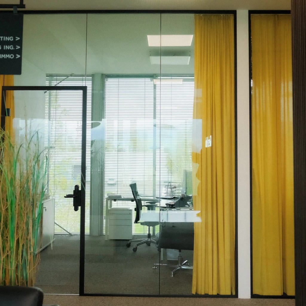 Private Office bei GlessHub: Glasfront, heller Arbeitsplatz mit senfgelbem Vorhang und viel Tageslicht