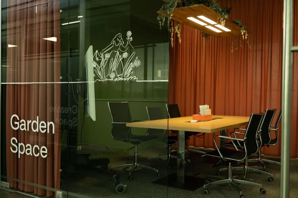 Garden Space Meetingraum im GlessHub: Konferenztisch, großer Bildschirm, Vorhänge und Glasfront mit Beschriftung